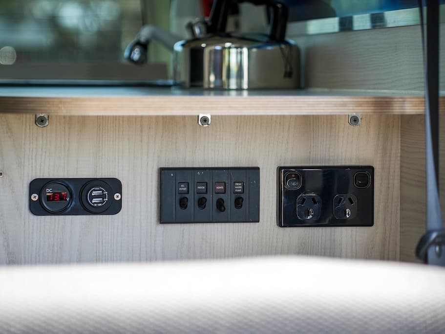 Twelve-volt switch panel labelled DC outlet, fridge, lights and fresh water pump, beside a USB socket and a double 230-volt outlet