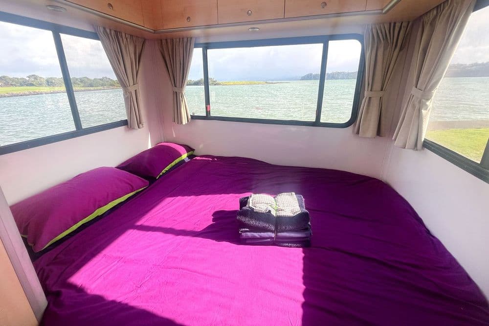Over-cab luton double bed made up with purple bedding and folded towels, windows either side