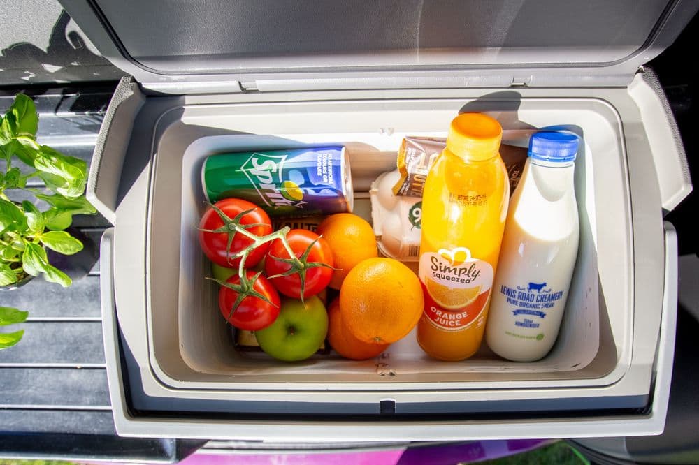 Open top-loading compressor fridge in the rear of the campervan, packed with fruit, vegetables and milk