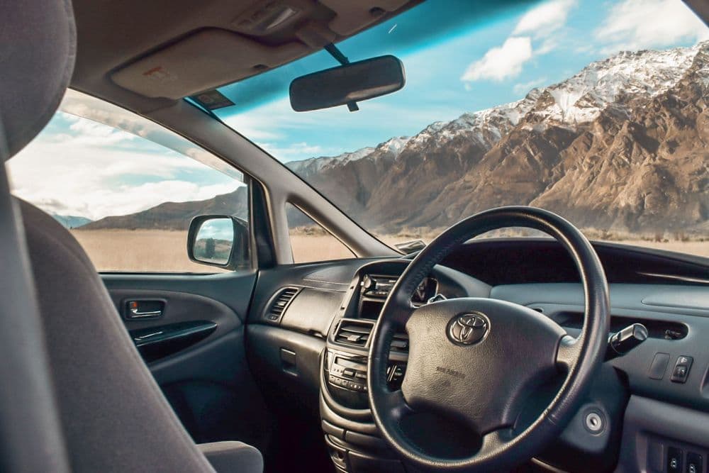 View across the Toyota steering wheel and dashboard towards snow-covered mountains through the windscreen